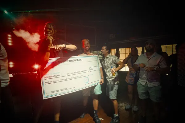 A group on stage in red light holding a giant novelty cheque