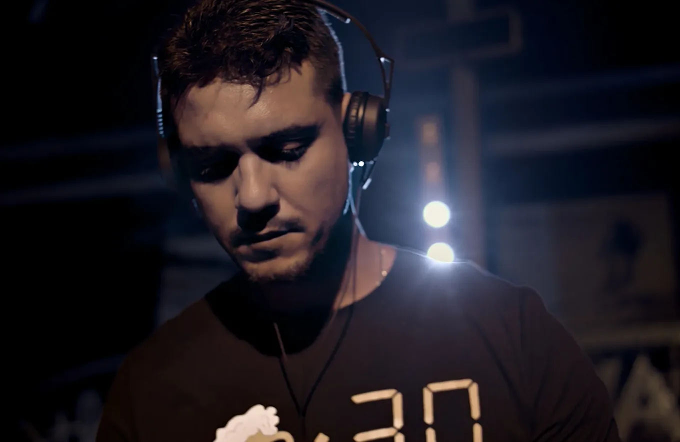 A DJ in headphones looking down at the decks under dim stage light