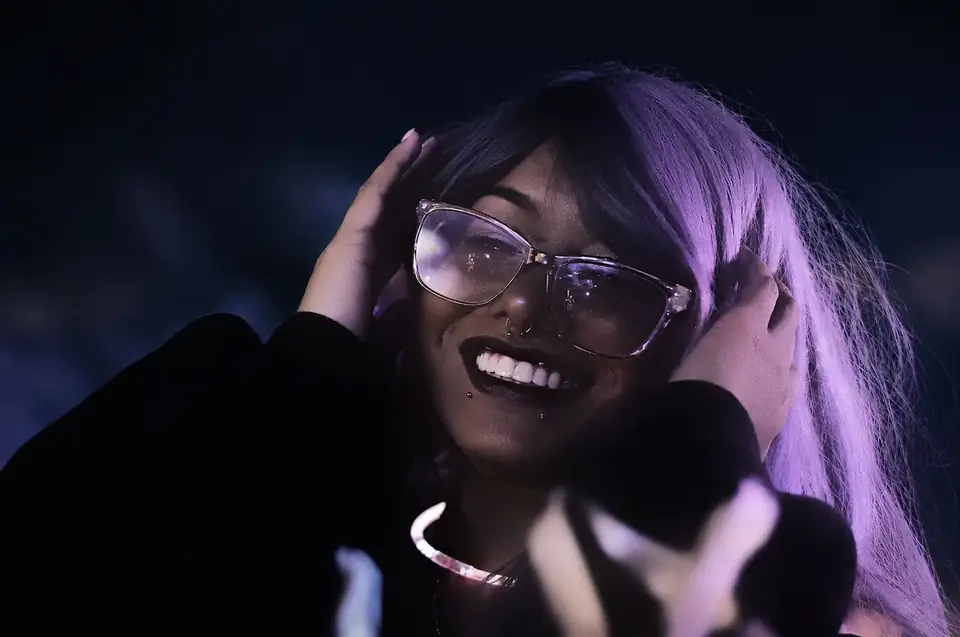 A woman in glasses laughing in purple light